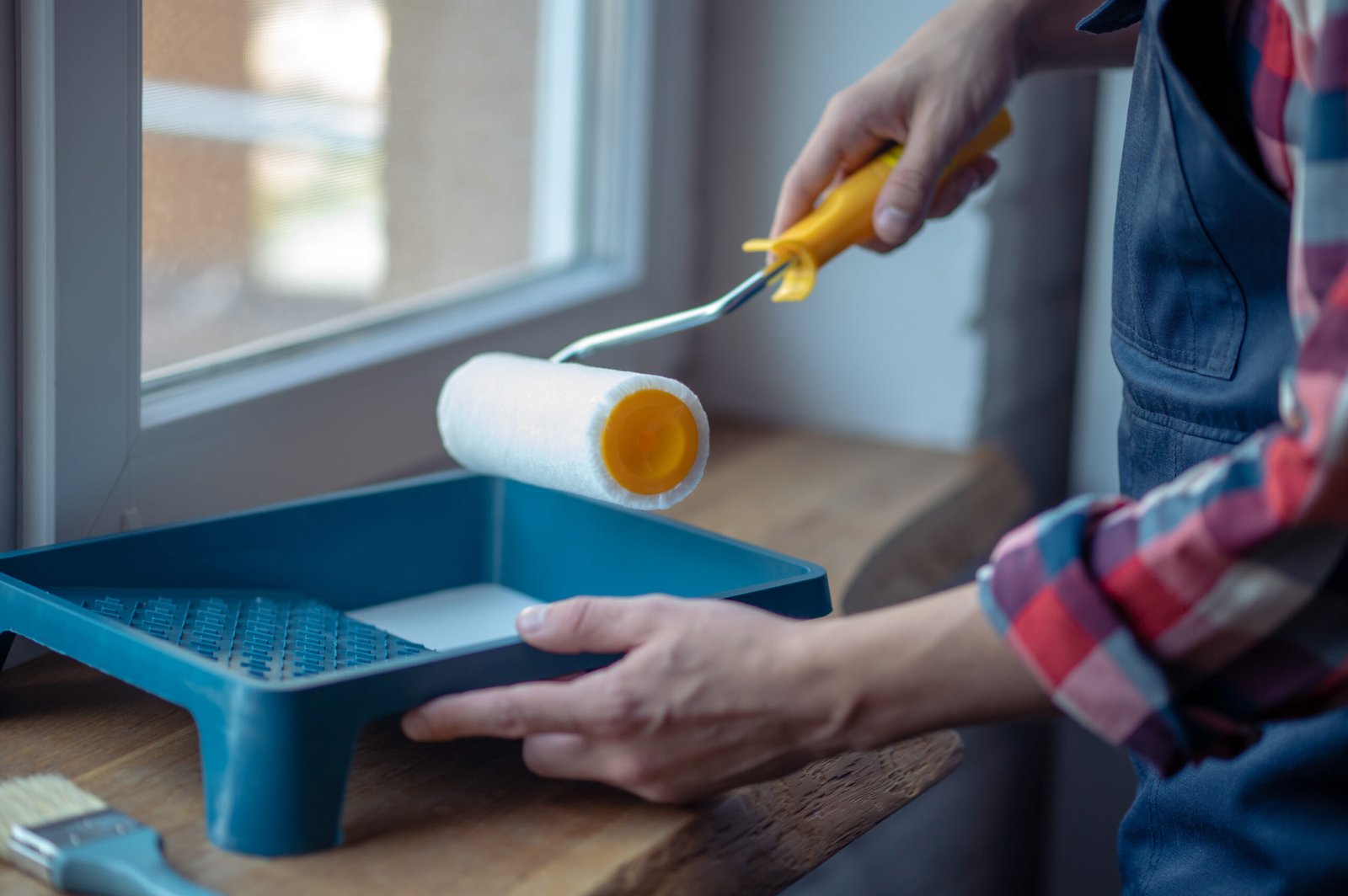 Cropped photo of a painter in workwear dipping the roller into the paint in the paint tray